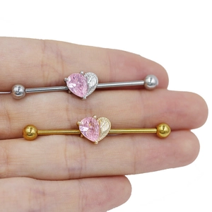 Detail shot of heart-shaped industrial barbell earrings with pink zircon and wing motifs