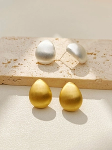 Detail of teardrop earrings featuring a brushed metallic finish in gold and silver