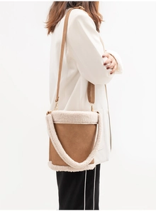 Detail of brown faux leather bucket bag featuring plush white faux fur trim and adjustable strap