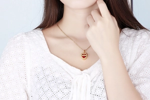 Detail of gold heart pendant necklace with red gemstone and MOM engraving on model
