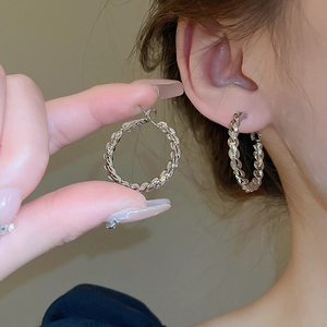 Minimalist silver-tone twisted hoop earrings with a polished metallic texture on a model