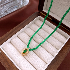 Green bead necklace with oval gold pendant on beige velvet inside a vintage wooden box