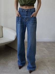 Detail of blue denim jeans featuring a unique V-shaped cross waistband and straight leg cut