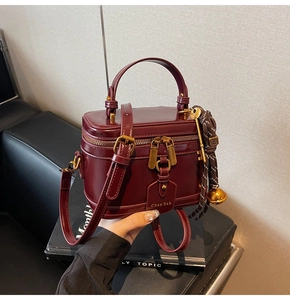 Close-up of burgundy bucket bag with gold zippers and decorative charms on a hand-held strap