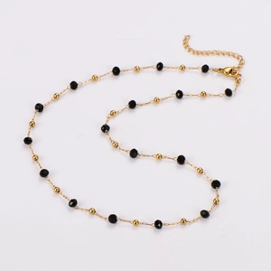 Gros plan du collier doré avec perles noires et fermoir mousqueton sur fond blanc