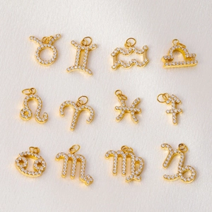 Set of 12 gold plated zodiac charms with micro paved zircons on beige satin