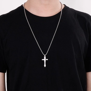 Gros plan d'un collier pendentif croix en argent porté par un mannequin homme sur noir