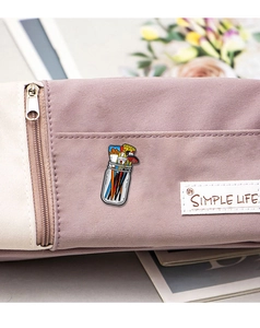 Macro detail of a colorful paintbrush jar enamel pin on a purple canvas bag surface