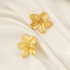 Elegante goldene Blüten-Ohrstecker mit gebürsteter Metallstruktur auf weißer Seide