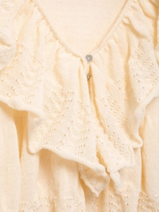Detail of cream knit sweater showing V-neck ruffles and delicate pointelle floral patterns