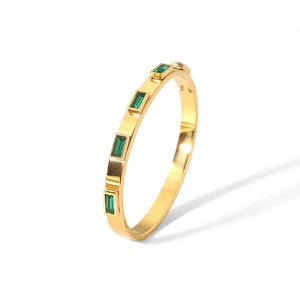 Detailed view of gold plated bangle with four rectangular green zircons on white background