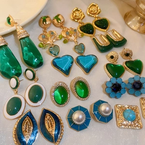 Flat lay of vintage green and blue heart-shaped earrings with pearls on white fabric