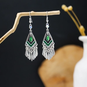 Detail of bohemian silver earrings with green resin and leaf tassels on a branch