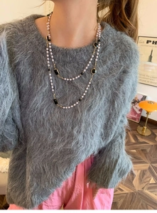 Detail of layered gold necklace with white pearls and black enamel charms on a grey sweater
