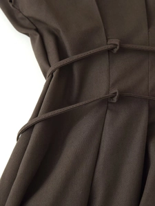 Detail of waist tie knot on a dark brown pleated dress with visible woven texture