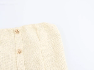 Nahaufnahme goldener Webknöpfe an einem beigen Tweed-Trägerlosenkleid mit Textur-Details