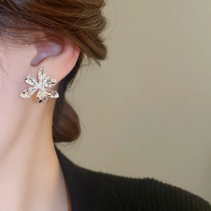 Detailed close-up of silver metal floral stud earrings on model with a textured finish