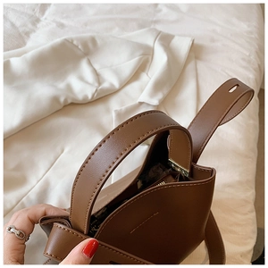 Close-up of brown leather bucket bag showing fine stitching and polished metal hardware