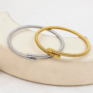 Detailed shot of gold and silver spring coil bracelets on a minimalist beige display stand