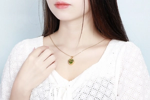 Close-up of gold heart necklace featuring a green gemstone pendant worn by a model