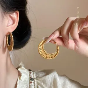Close-up of bohemian round rattan woven hoop earring with vintage gold hook on ear