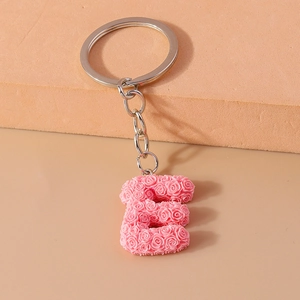 Macro shot of letter E keychain featuring pink miniature rose textures on a beige pedestal