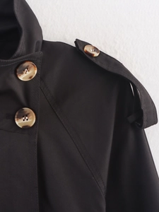 Detailed close-up of shoulder epaulettes and tortoise shell buttons on a black trench coat
