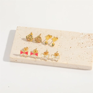 Set of four gold bow and zircon stud earrings on a beige stone display board