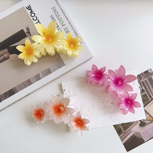 Three oversized matte flower hair claws in yellow and pink hues on a white desk
