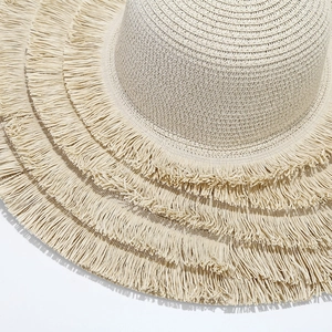 Close-up of beige straw sun hat showing tiered fringe trim and fine woven texture