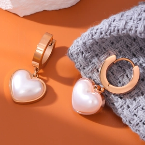 Elegant rose gold heart earrings with white pearl inlay on orange and grey background