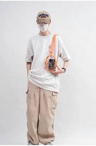 Detailed view of an orange transparent PVC crossbody bag worn by a model in a studio