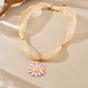 Macro shot of gold-plated stainless steel daisy pendant with beige organza ribbon strap