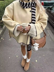 Detail of beige wool shawl coat with black hand-stitched embroidery and striped scarf