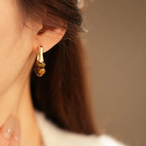 Detailed shot of gold hoop earrings with tiger eye stone beads on a female model