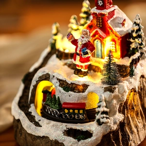 Close-up of a lit Christmas snow house with Santa and moving train resin scene