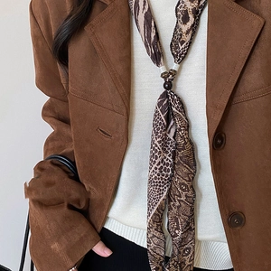 Nahaufnahme des schmalen Chiffon-Schals mit Leopardenmuster und Perlen auf braunem Blazer