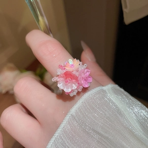 Dettaglio dell'anello in perline di resina a fiori rosa e bianchi indossato con sfondo sfocato