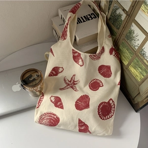 Detail of canvas tote bag with red seashell print on a minimalist white desk