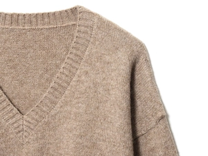 Détail d'un pull en maille beige à col en V avec finition côtelée et texture douce
