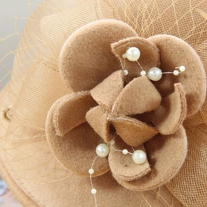 Détail d'une fleur en feutre de laine avec perles blanches et voilette sur chapeau