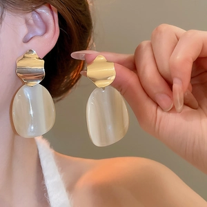Detail view of gold wavy metal and milky white oval pendant earrings on model ear