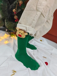 Detail von grünen Weihnachts-Stricksocken mit 3D-Rentierpuppen vor festlicher Kulisse