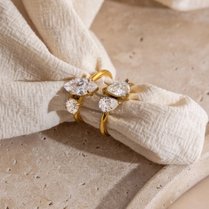 Detail of two 18K gold plated rings with marquis and teardrop zirconia on stone surface