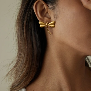 Gros plan détaillé d'une boucle d'oreille libellule en or mat 18K portée par un mannequin
