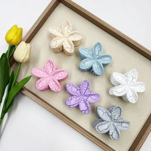 Set of six colorful plumeria flower hair claws in matte finish on a wooden tray