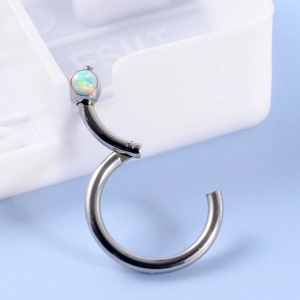 Macro shot of curved stainless steel piercing jewelry with opal stone setting