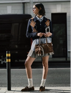 Detail of vintage preppy style plaid knit cardigan paired with striped shirt and pleated skirt
