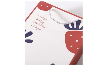 Detail of white paper gift bag with red strawberry prints and silver woven handles