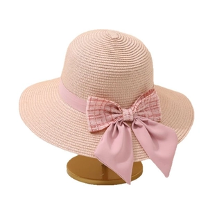 Pink straw sun hat with checkered bow decoration on gold display stand for beach vacations